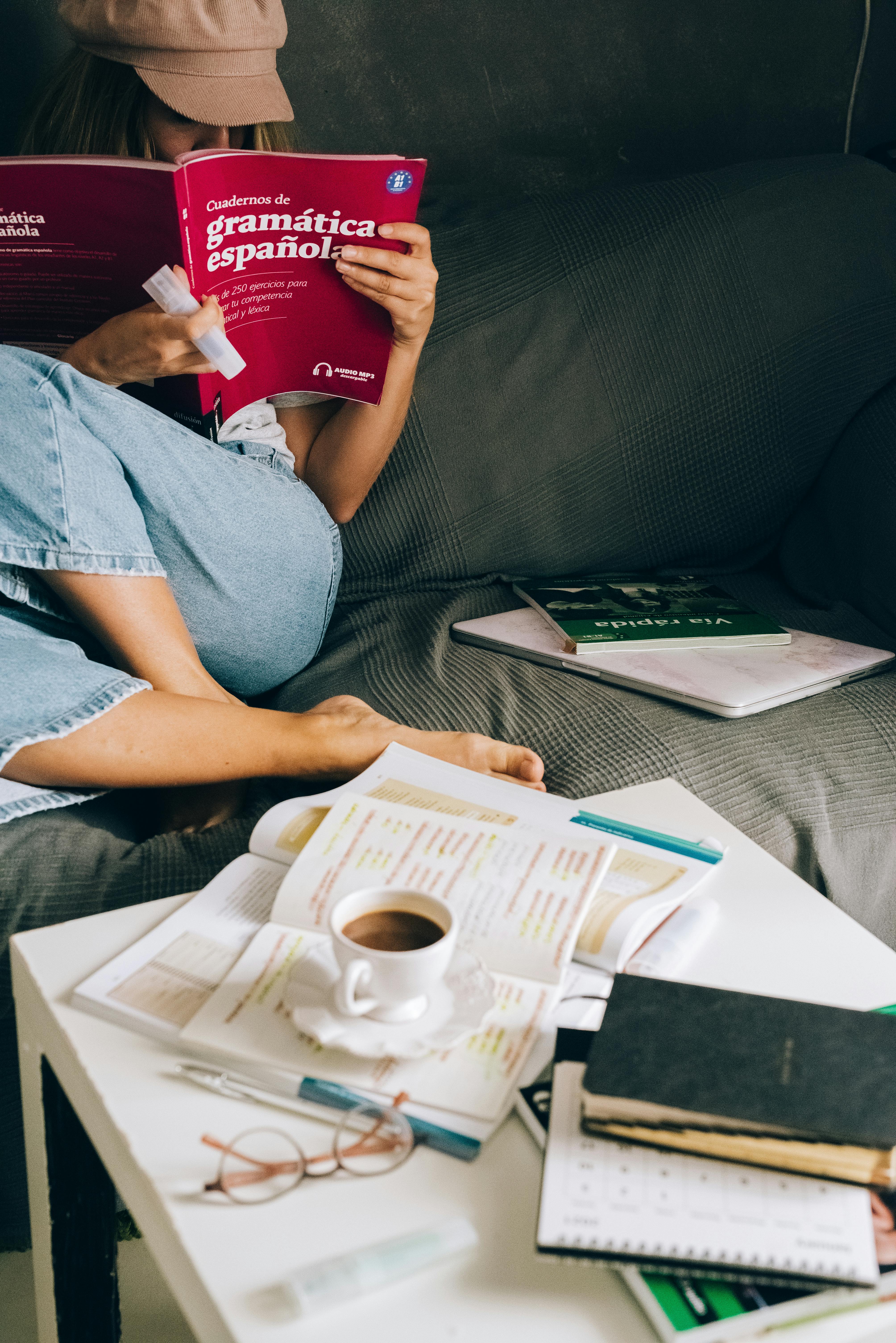 Woman studying Spanish grammar at home with coffee, books, and notes.